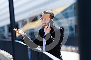 Businessman in a rage shouts at mobile phone outside, upset, hate