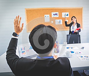 Businessman raised hand in meeting while female office worker is presenting work in meeting room