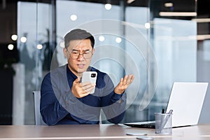 Businessman reading bad news online from phone, asian man disappointed and sad looking at smartphone screen, man in
