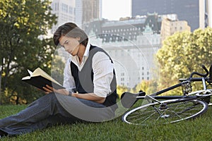 Businessman Reading Book By Bicycle In Park