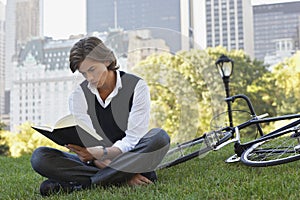 Businessman Reading Book By Bicycle In Park