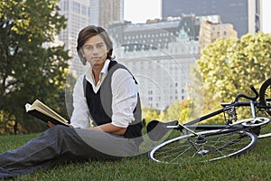 Businessman Reading Book By Bicycle In Park