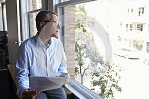 Businessman Reading Document Sitting By Office Window