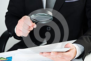 Businessman reading documents with magnifying glass