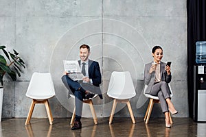 Businessman reading newspaper while asian businesswoman using smartphone in