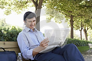 Businessman Reading Newspaper On Bench
