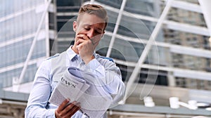 Businessman reading newspaper feeling serious standing in urban background. Handsome men holding newspaper in his hand with