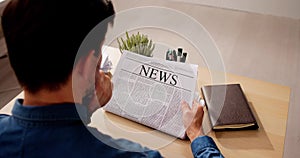 Businessman Reading Newspaper At Office Desk