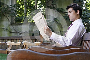 Businessman Reading Newspaper On Park Bench