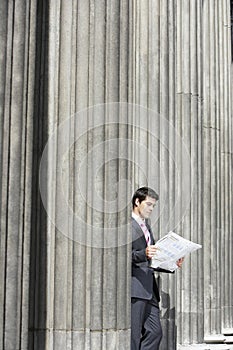 Businessman Reading Newspaper By Pillar