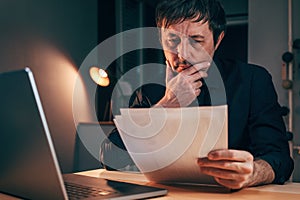 Businessman reading paper document report in business office, exhausted adult male working overtime