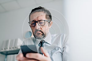 Businessman reading worrisome text message on mobile phone