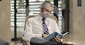 A businessman reads a notepad sitting in the hotel lobby or office.