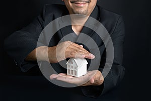 Businessman real estate realtor or house insurance agent making a protecting hands gesture over the house.