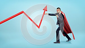 A businessman in a red superhero cape throwing punches at a red statistic arrow pointing upwards.