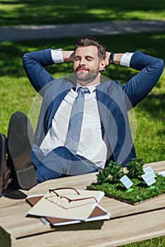 Businessman relaxing while sitting at table with sun batteries layout, glasses and noteboks, crossed lags and put hands photo