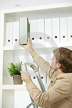 Businessman removing green folder from shelf