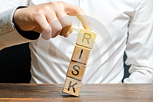 Businessman rescues with his finger a tower of cubes with the word Risk from falling Risk management, cost assessment, business