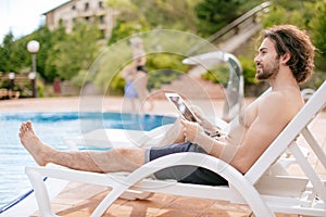 Businessman resting on sunbed near swimming pool while working remotely at laptop computer connected to wireless