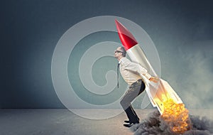 Businessman with rocket on his back ready to take off