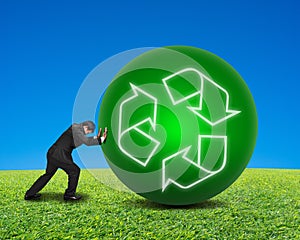Businessman rolling large ball with recycling symbol on green fr