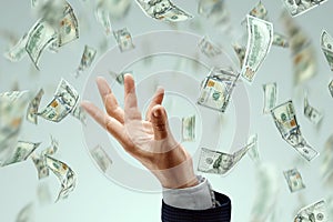 Businessman`s hand catches falling dollars on a light background. The concept of investments, dividends, interest, bank deposits