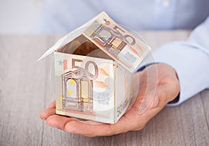 Businessman's hand holding house made of euro notes