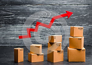 A businessman`s hand holds a red arrow up above cardboard boxes folded incrementally. Sales growth and increase in exports