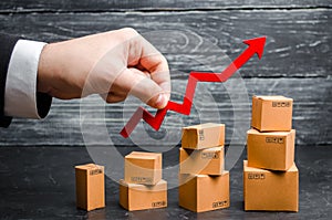 A businessman`s hand holds a red arrow up above cardboard boxes folded incrementally. Sales growth and increase in exports photo