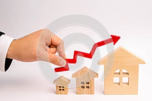 Businessman`s hand holds the red arrow up above the houses. The concept of growth in demand for real estate. Increase in the valu