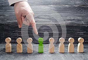 A businessman`s hand points to a green wooden human figure. The concept of the search for workers, management of human resources.