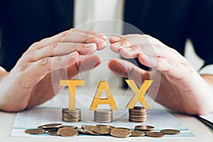 Businessman\'s hand is protecting letters with the word tax on a coin. Tax concept