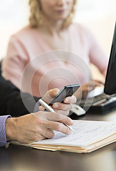 Businessman's Hand Using Mobile Phone At Desk