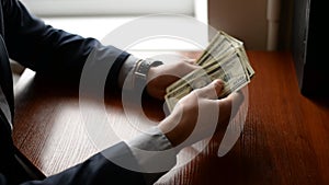 A businessman`s hands counting hundred dollar bills at a table. hands with watch and dollars on wood table. finance concept.