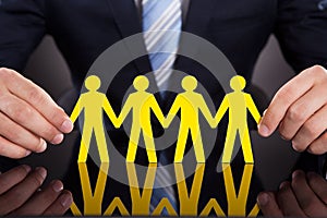 Businessman's hands holding paper people chain on desk