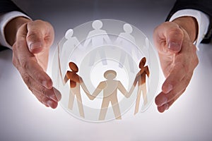 Businessman's hands protecting team of paper people on desk