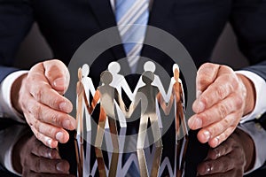 Businessman's hands protecting team of paper people on desk