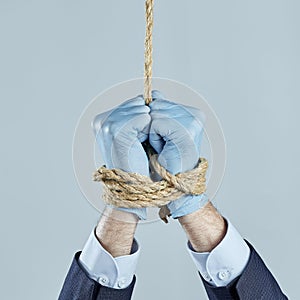 The businessman`s hands in rubber gloves are tied with a rope and suspended on gray background. It is forbidden to work
