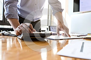 Businessman`s hands using calculator and Financial data analyzing on wooden desk at the office