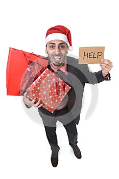 Businessman in Santa Claus hat holding shopping bags asking for help with cardboard sign worried