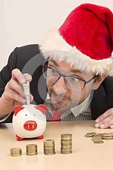 Businessman with Santa hat inserting one dollar bill into piggy bank