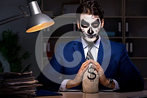 The businessman with scary face mask working late in office