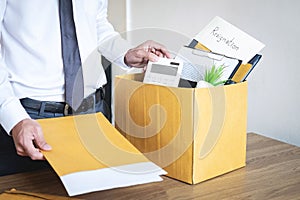 Businessman sending letter will being resignation and carrying packing belongings company and files into brown cardboard box,