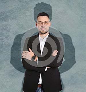 Businessman and shadow of strong muscular man behind him on grey wall. Concept of inner strength