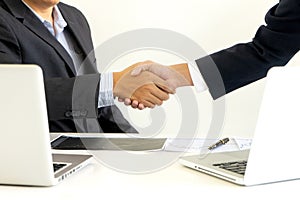 businessman shake hand at the office table between computer