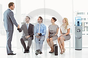 Businessman shaking hands with man besides people waiting for interview