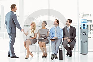 Businessman shaking hands with woman besides people waiting for interview