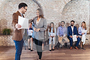 Businessman shaking hands with woman besides people waiting for job interview