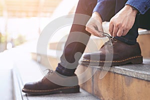 Businessman in a shirt jeans tie up shoelace on wearing brown leather shoes sitting staircase background. Men`s style.