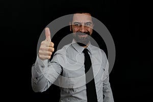 A businessman in a shirt and tie with a smiling face on a black background makes the thumb up gesture.